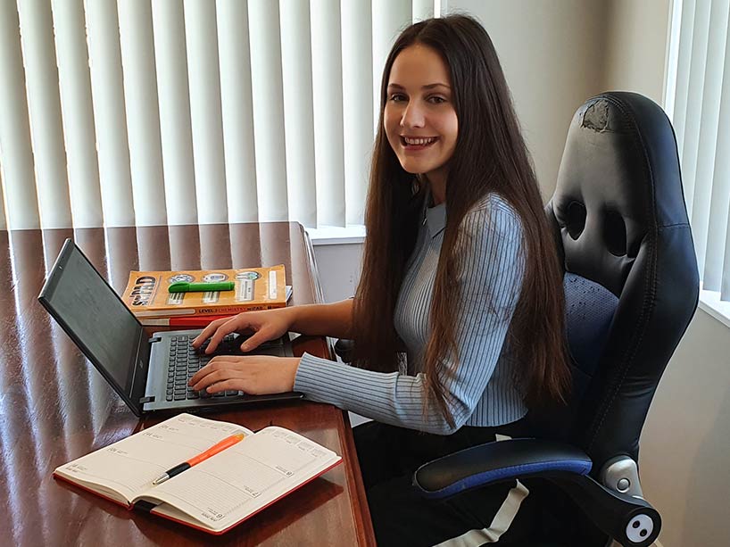 Student Savannah Mastrodicasa smiles at the camera while sitting at a table with her laptop