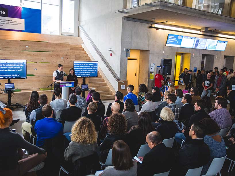 A crowd listening from seats as two people speak at a podium. 