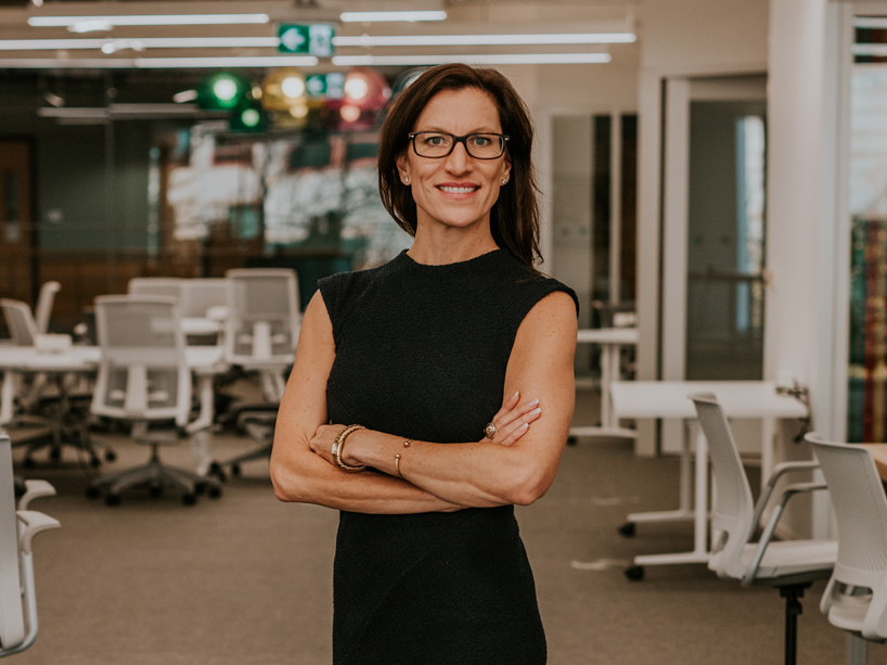 Laurel Walzak stands with arms crossed in a long black dress, smiling.