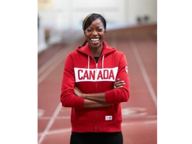 Nicole Forrester stands on the track smiling, wearing a red sweatshirt that says “Canada”.