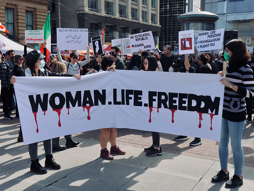 Young women holding a banner that reads “Woman, Life, Freedom”.