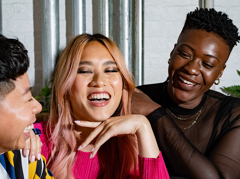 Three people laughing together on a couch.