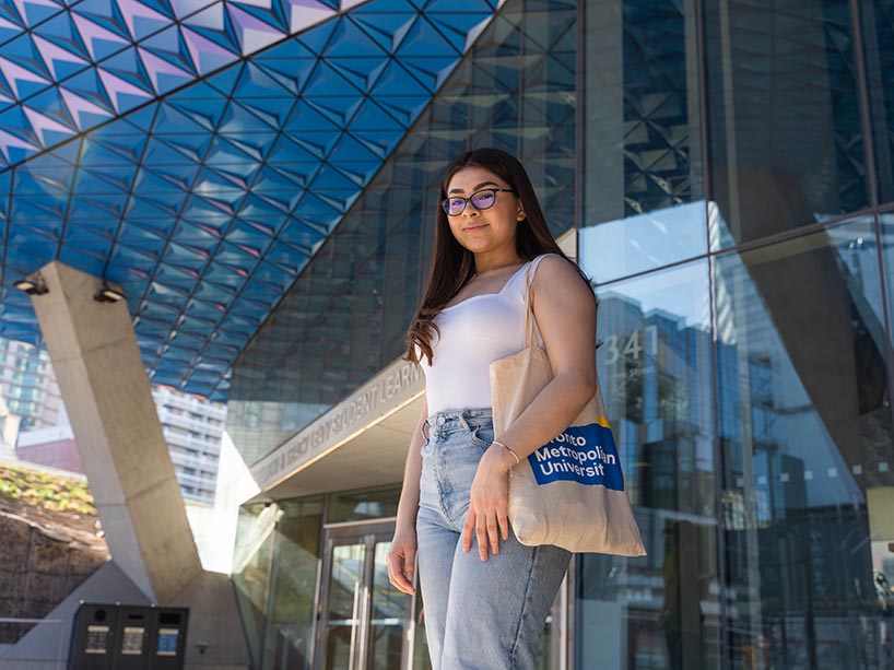 Rebeka Salazar in front of the SLC with a Toronto Metropolitan University tote.