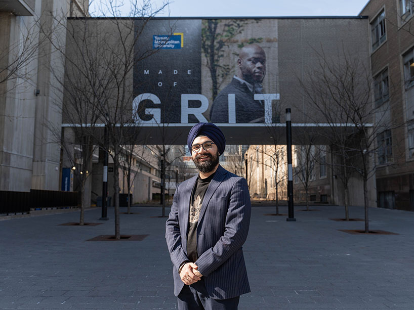 Jasmann Singh Narang in a blue blazer standing in front of a Grit campaign poster.