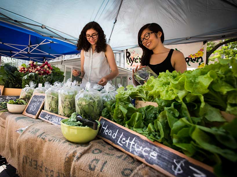 Two people selling vegetables behind a table.