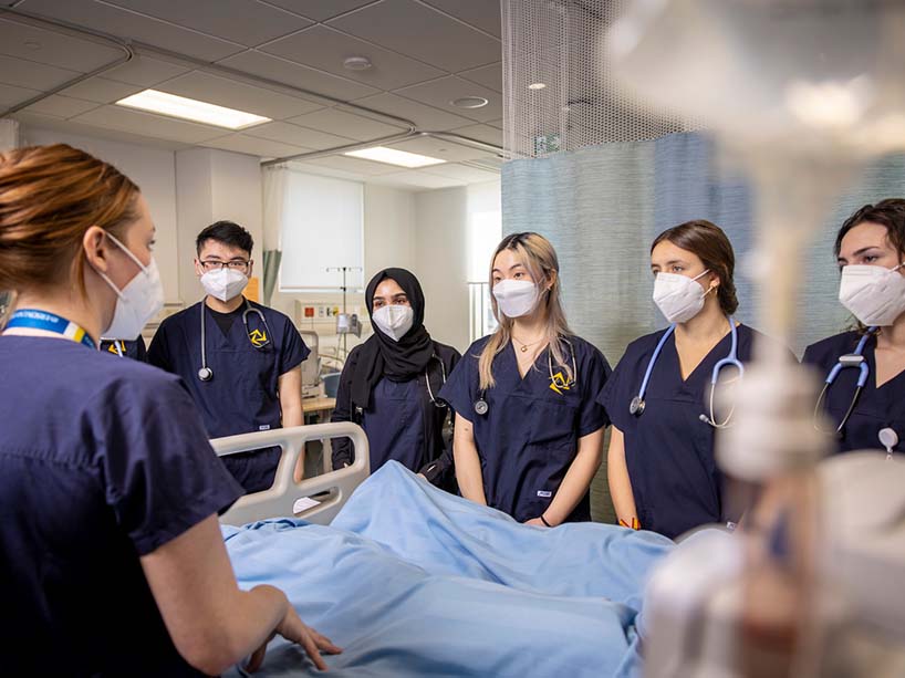 A group of nursing students gather around a hospital bed as they learn