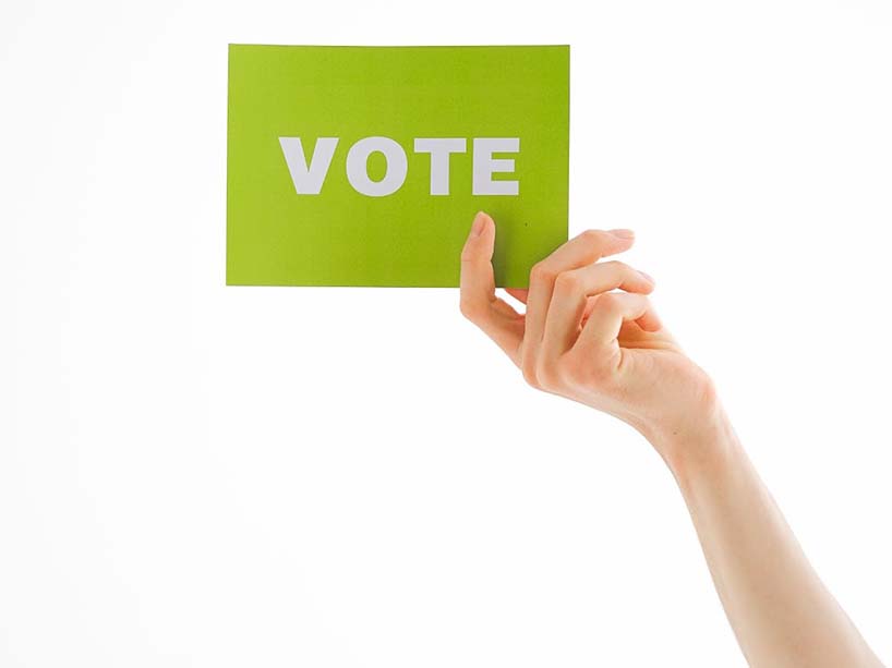 A hand holding up a green sign that reads ‘Vote’.