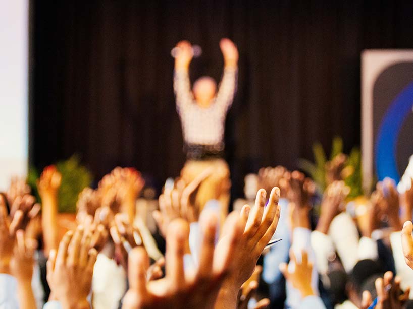 Person on a stage in front of a crowd with hands raised.