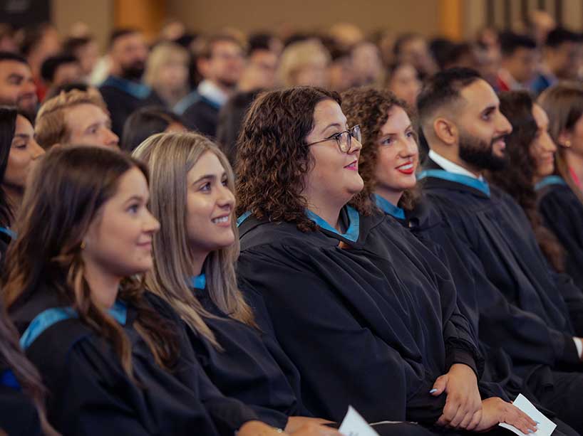 Graduates smiling and looking up at the stage. Photo credit: Kenya-Jade Pinto.