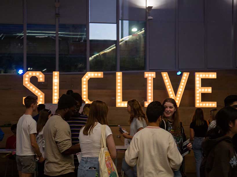 Students mingling in front of a lit-up SLC Live sign. 