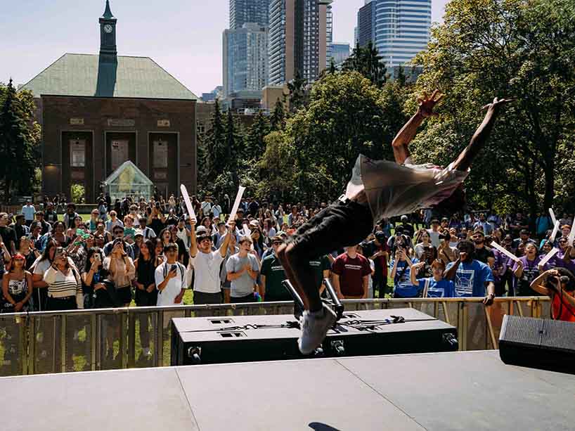 Performer doing a backflip on stage in front of a crowd of students.