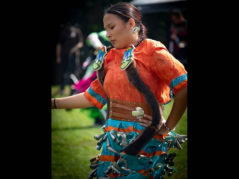 A young woman dances in a traditional jingle dress.