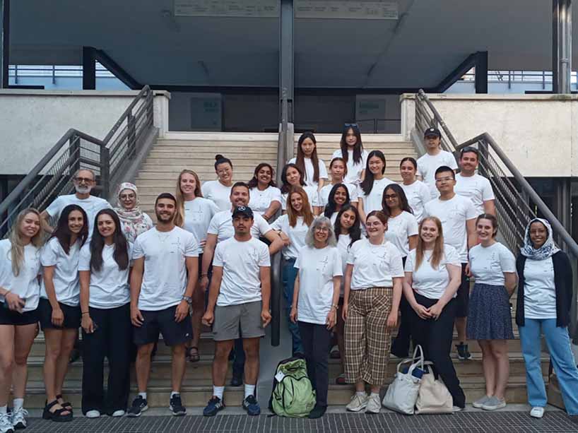 A group of students and their two professors stand on a flight of stairs wearing the same white shirt.