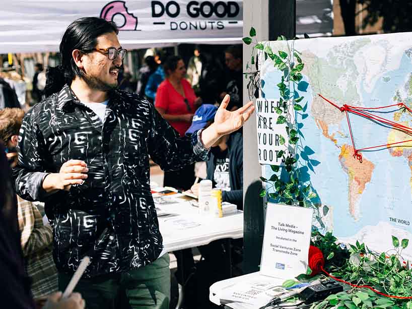 Transmedia Zone member Adam Chen stands at left, pointing toward a map, which is part of his installation for his startup, The Living Magazine.