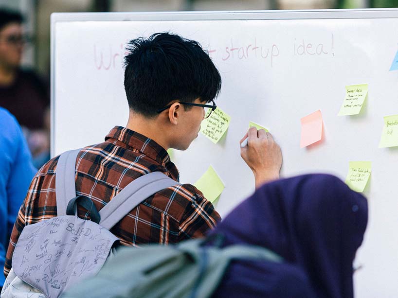 A student writes his startup idea on a white board with sticky notes.