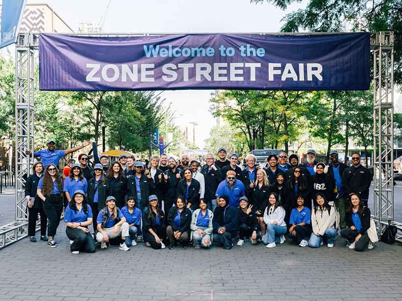 Group of people under a large street fair sign stretching across Gould Street. 