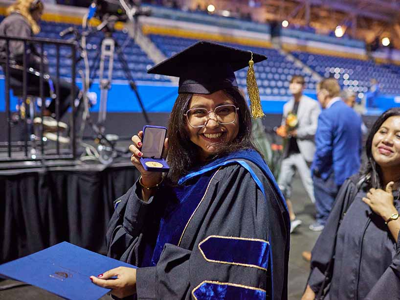 Fateen Basharat, a PhD graduate in physics, flashes a smile at the camera as she holds up her TMU Gold Medal at Fall 2023 convocation ceremonies.