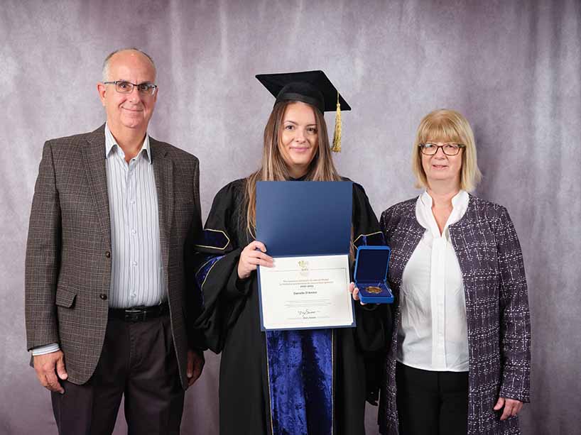Danielle D’Amico, recipient of both a TMU Gold Medal and the Governor General Gold Medal Award, stands holding her awards and her degree with her parents.