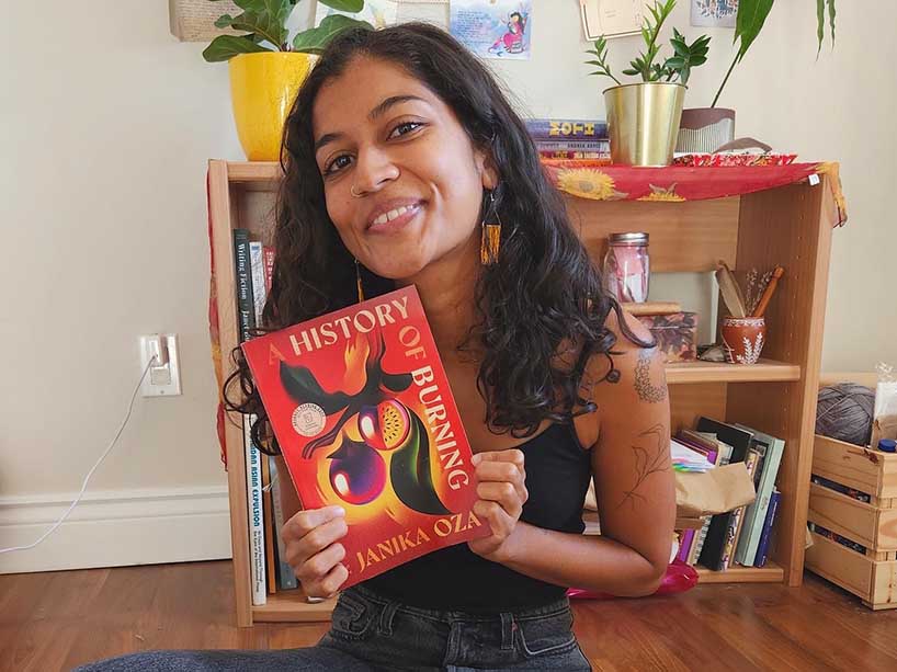 A young woman opens a box of books and holds one up, smiling.