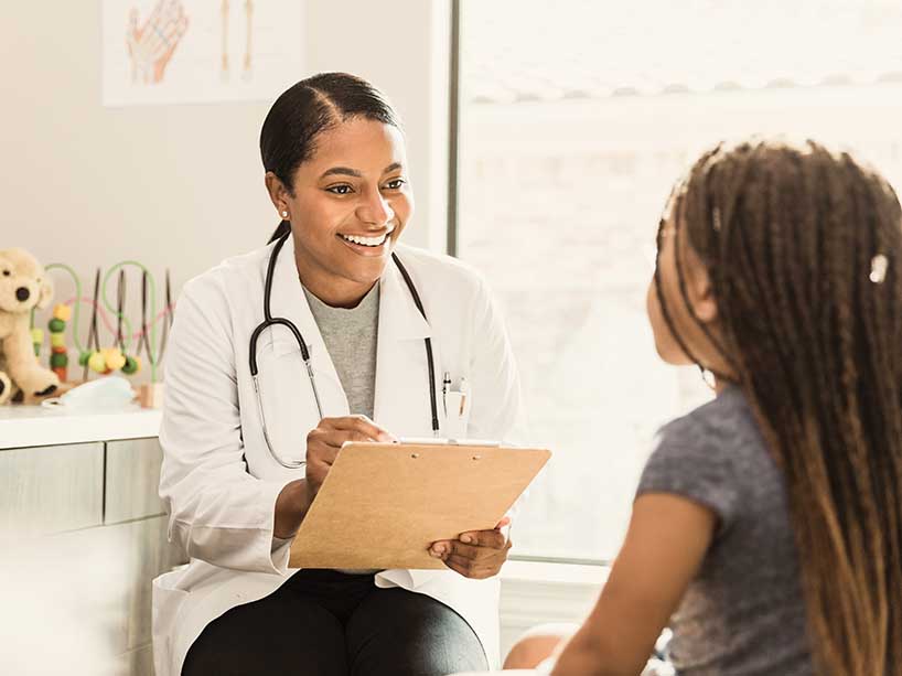 Black physician consults with a young Black child in a doctor’s office.