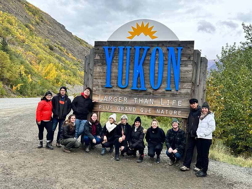 A group of students gathers in front of the Yukon welcome sign.