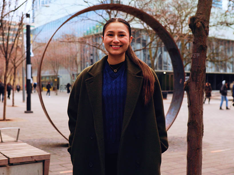 Saije Catcheway stands outside on the TMU campus smiling. 