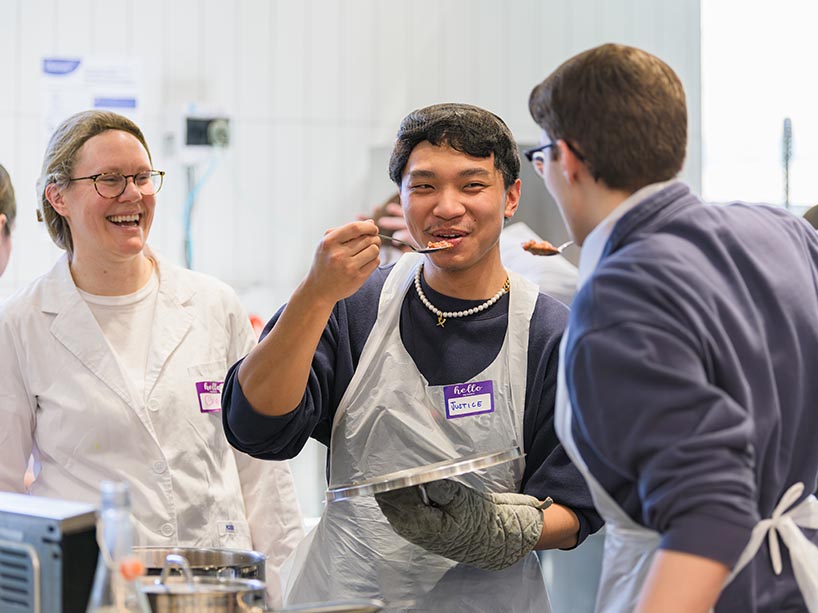 Two students try food while a nutrition student looks on