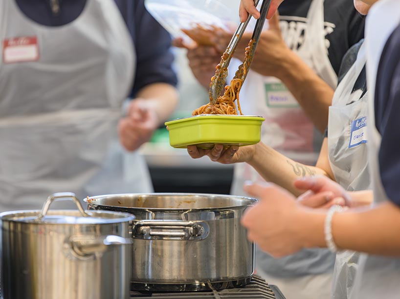 Someone adds pasta to a container