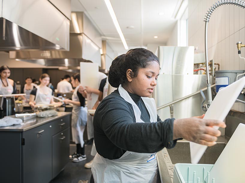 A student washes dishes in TMU’s food lab