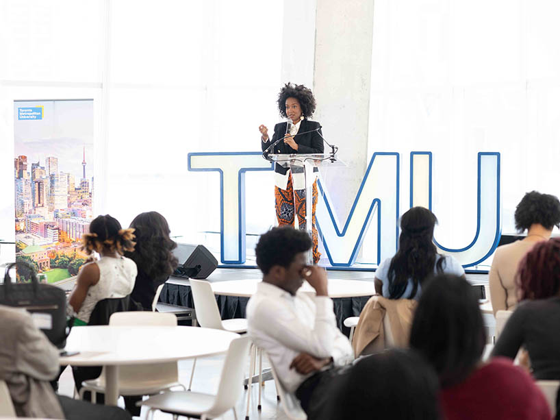 Amanda Parris on a stage with a TMU sign, addressing a room of people.