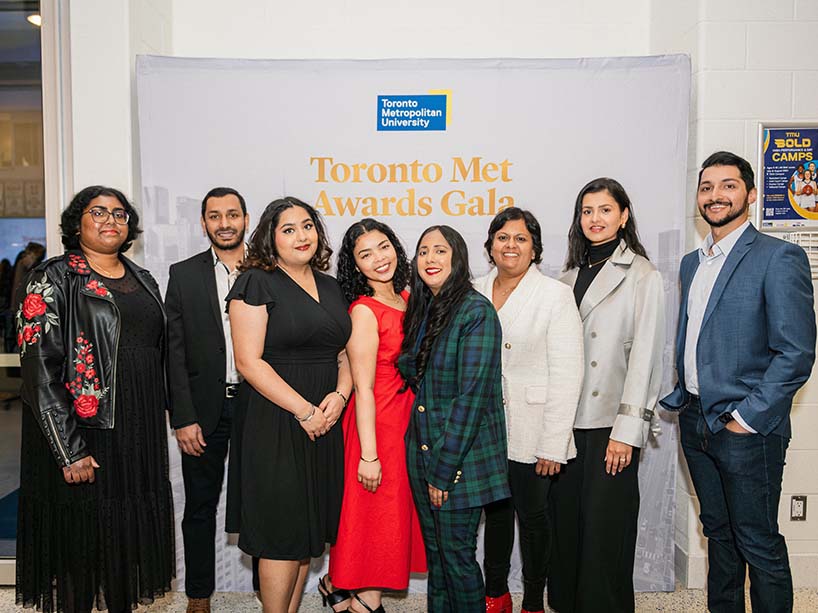 Guest of recipient, Riaz Ahmed, Muskaan Baraech, Nikole Lyn, Arleana Rajkumar, Usha Srinivasan, Prabaarja Bedi and Fardan Khan pose in front of a ‘Toronto Met Awards Gala’ banner.