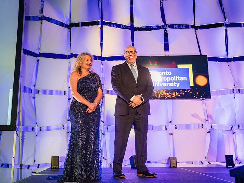 Roberta Iannacito-Provenzano and Mohamed Lachemi stand on a stage, illuminated by blue light.