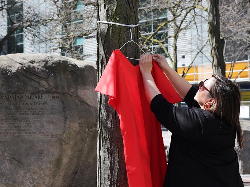 A community member reaches to hang a red dress on a hanger in a tree.