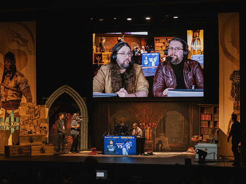 Two commentators of the event appear on a screen over the stage.
