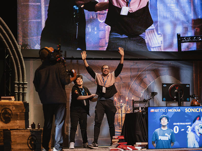The winner of the Mortal Kombat 1 Final Kombat World Championship raises their arms up in celebration while on stage at the event.
