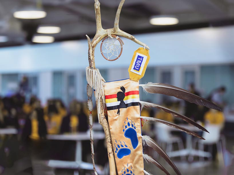 Part of the Eagle Staff, including beaded TMU letters, three feathers and red, yellow, white and black ribbons