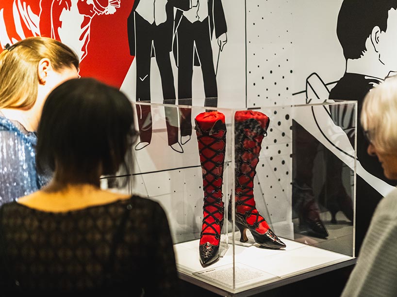 Exhibit attendees view a pair of red and black knee-high heeled boots 