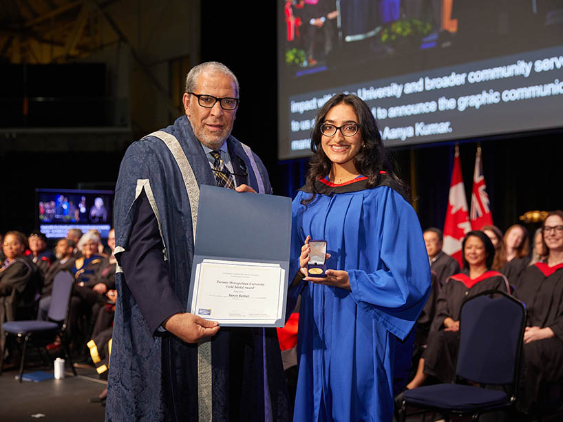 A man holding a certificate and a woman holding a gold medal pose for a photo at a Toronto Metropolitan University convocation ceremony.