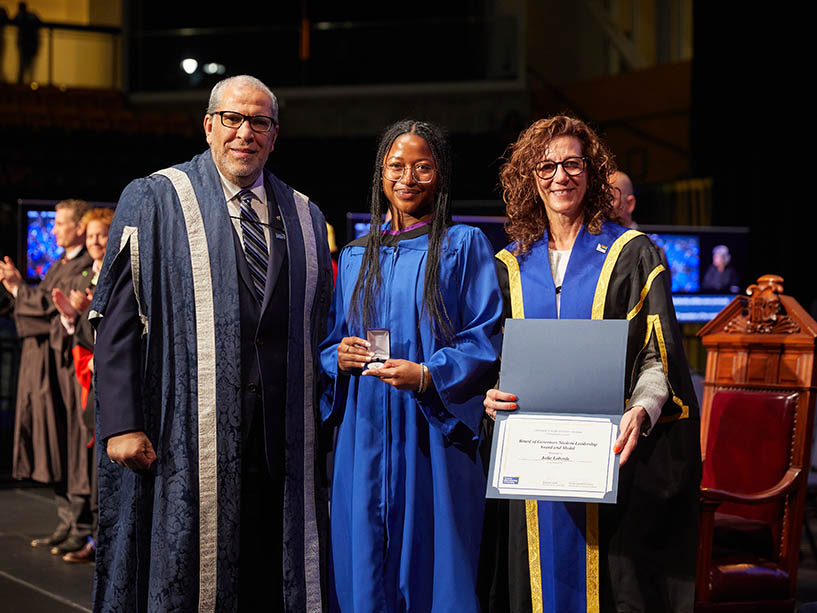 Three people wearing academic regalia pose for a photo after a Toronto Metropolitan University convocation ceremony.