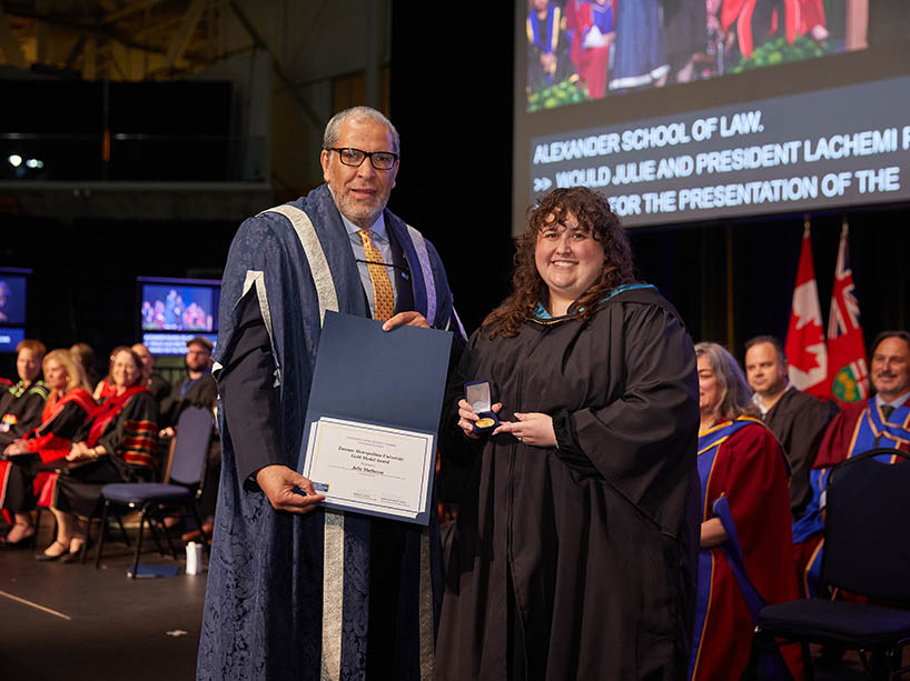 A man holding a certificate and a woman holding a gold medal pose for a photo at a Toronto Metropolitan University convocation ceremony.