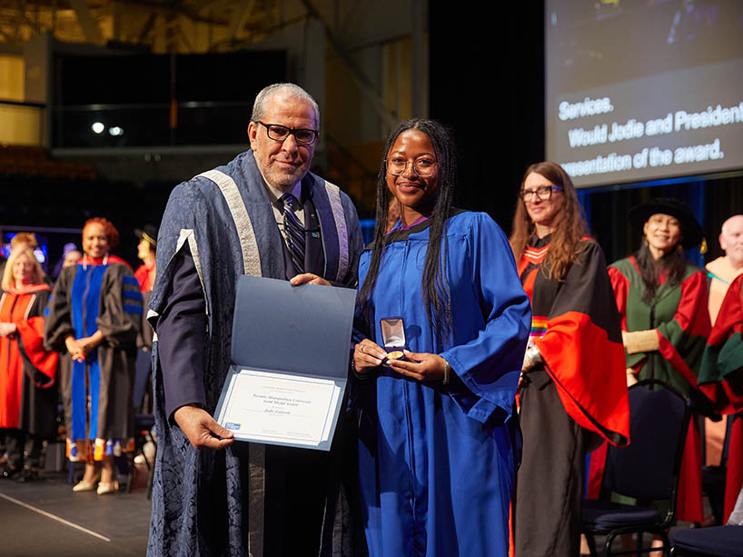 A man holding a certificate and a woman holding a gold medal pose for a photo at a Toronto Metropolitan University convocation ceremony.