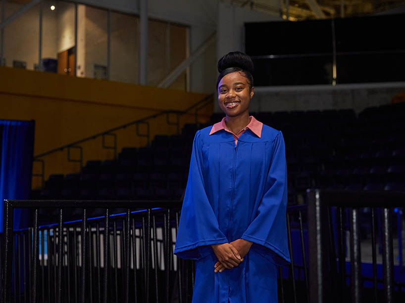 A woman wearing academic regalia waits to cross the stage at a Toronto Metropolitan University convocation ceremony.