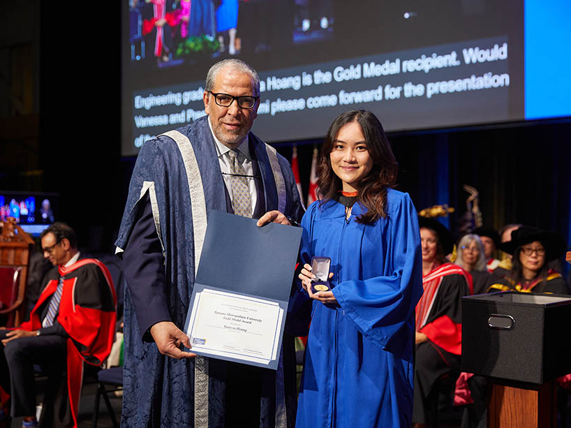 A man holding a certificate and a woman holding a gold medal pose for a photo at a Toronto Metropolitan University convocation ceremony.