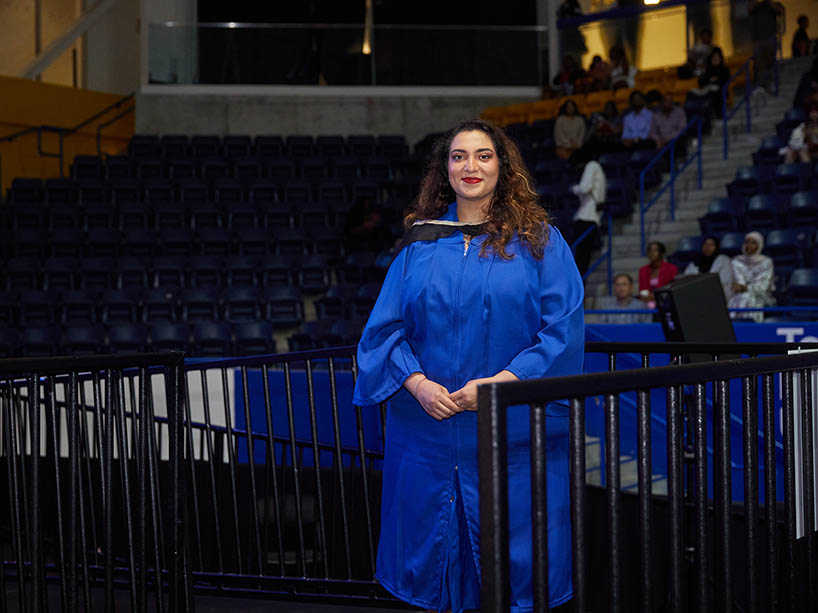 A woman wearing academic regalia waits to cross the stage at a Toronto Metropolitan University convocation ceremony.