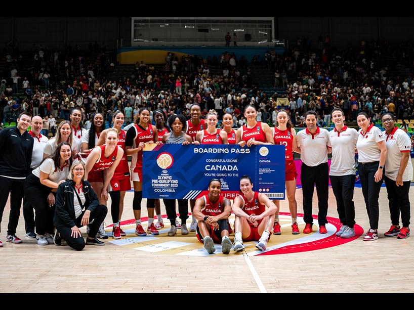 The Canadian women’s national basketball team poses for a group photo on a basketball court.