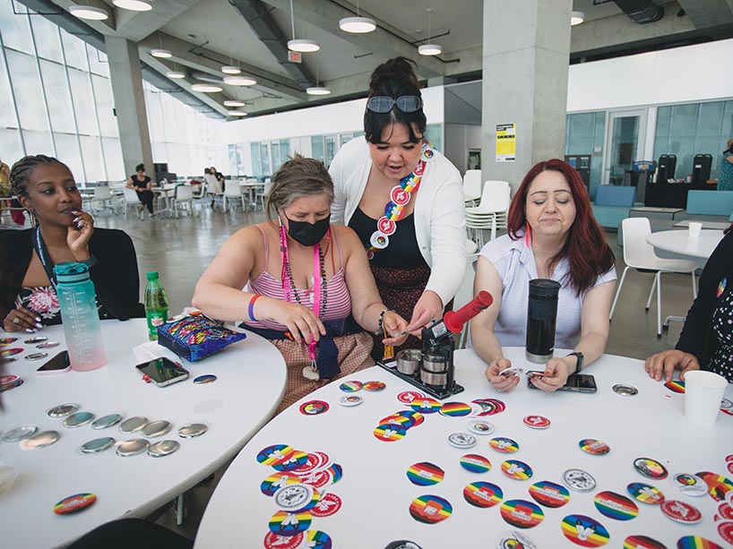 A group of community members sit at a table together making buttons.