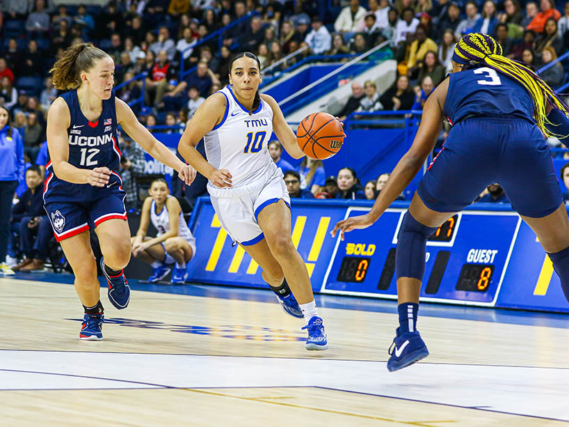 A TMU Bold player dribbles the ball down the court past an opponent.