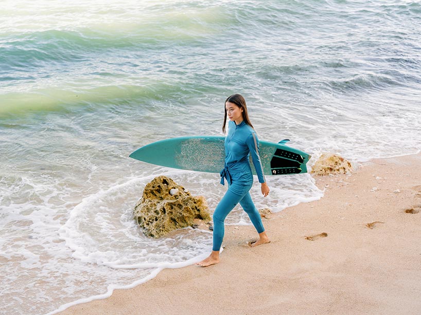 Young woman wearing skirted rash guard and leggings walking along a beach an holding a surfboard