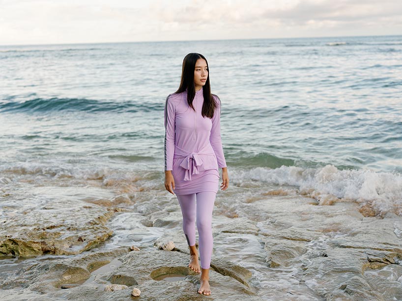 Young woman models a pink coloured full coverage swimsuit on the beach