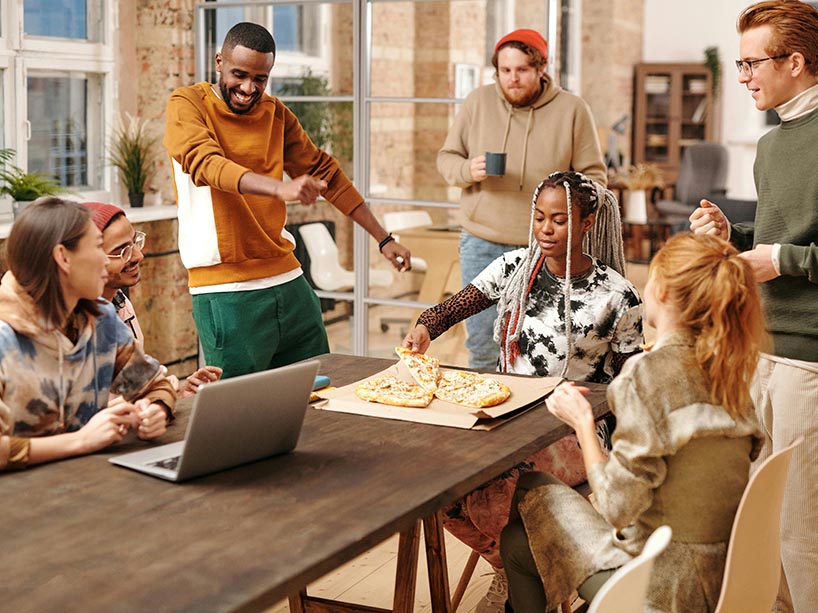 Young people gathered around a table sharing a pizza.